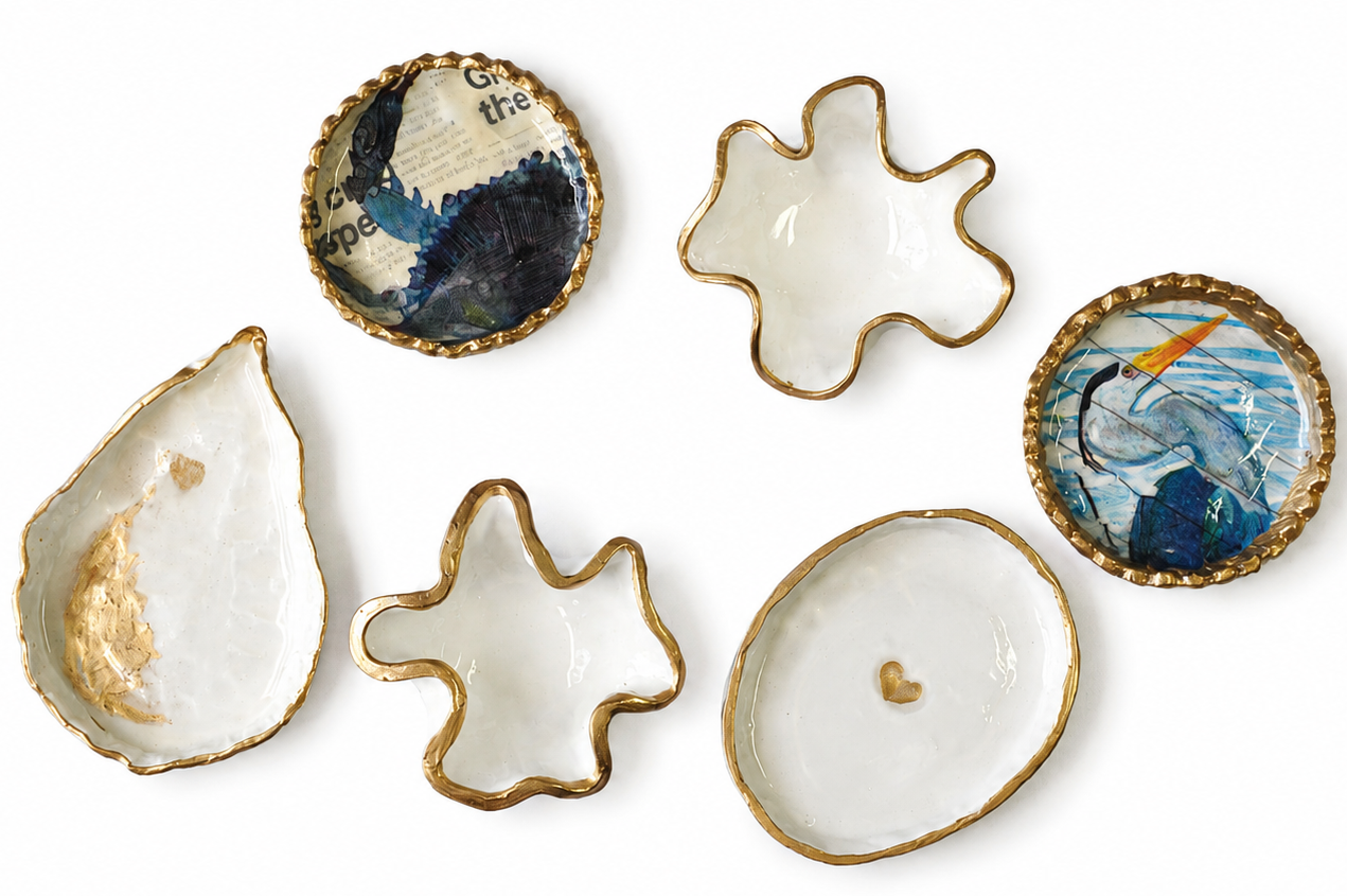 Six small decorative dish holders with organic, shell-like shapes and gold-trimmed edges, arranged on a plain white background. Four are plain white with gold edging, while two feature blue and white nautical artwork with a gold rim.